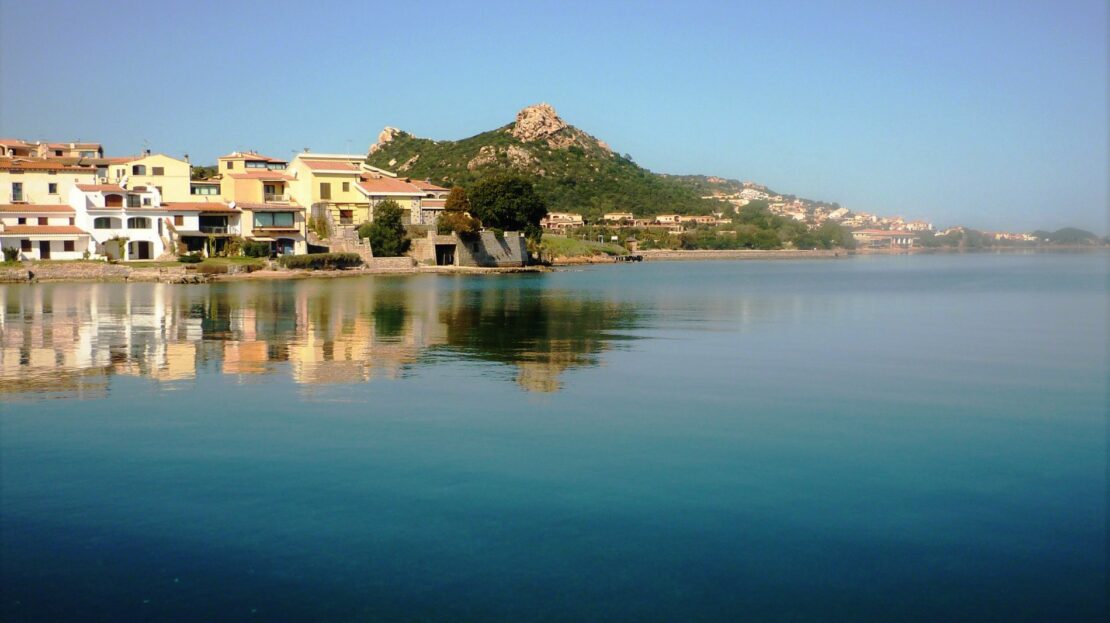 un panorama del mare nel golfo di Cannigione, con il mare blu e delle case vicino la riva sulla sinistra.